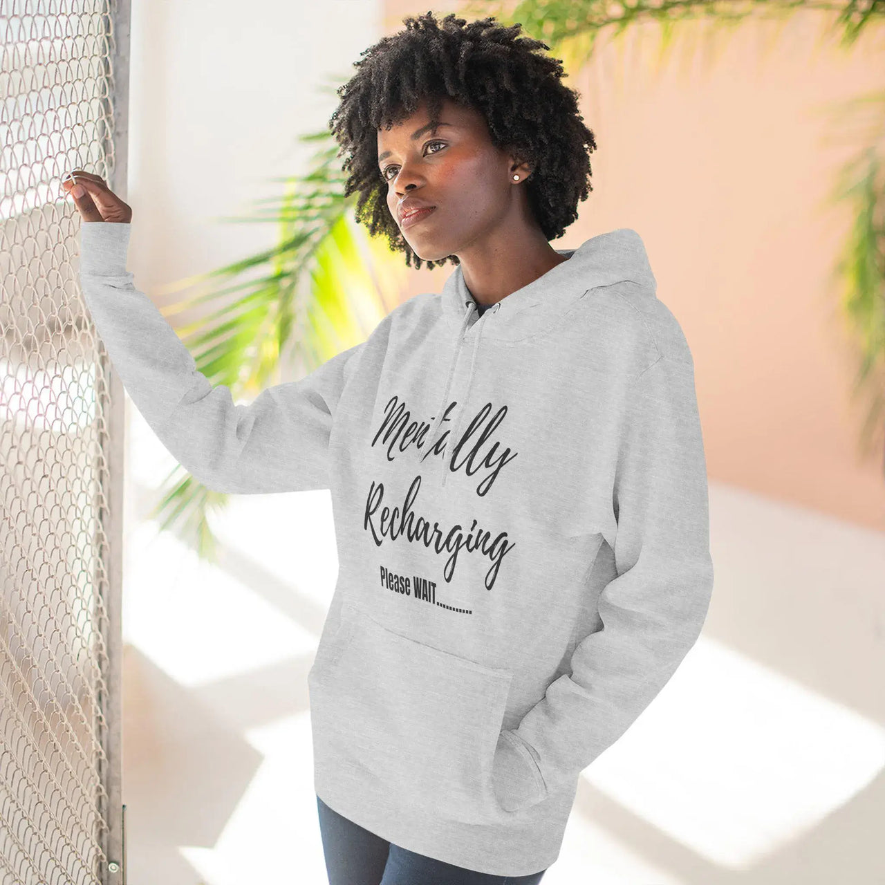 Person wearing a gray hoodie with text, standing indoors with plants in the background