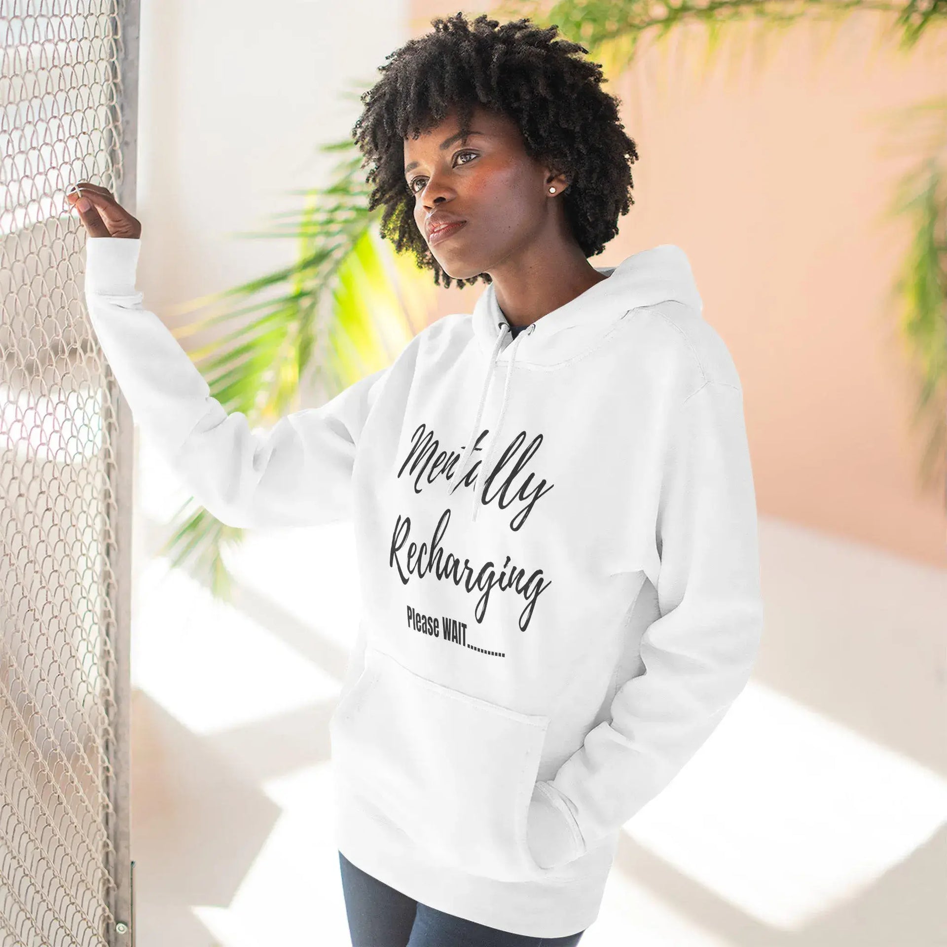 Person wearing a white hoodie with text, standing indoors with plants in the background