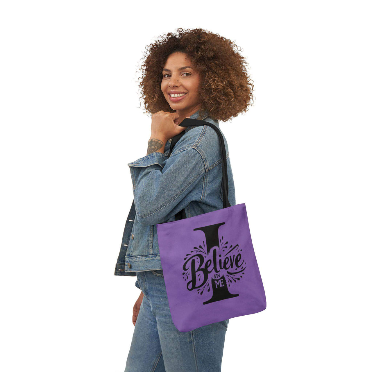 Woman holding a purple tote bag with 'I Believe' design on a white background
