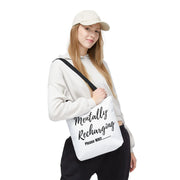 Person holding a white tote bag with text, wearing a white hoodie and cap on a white background