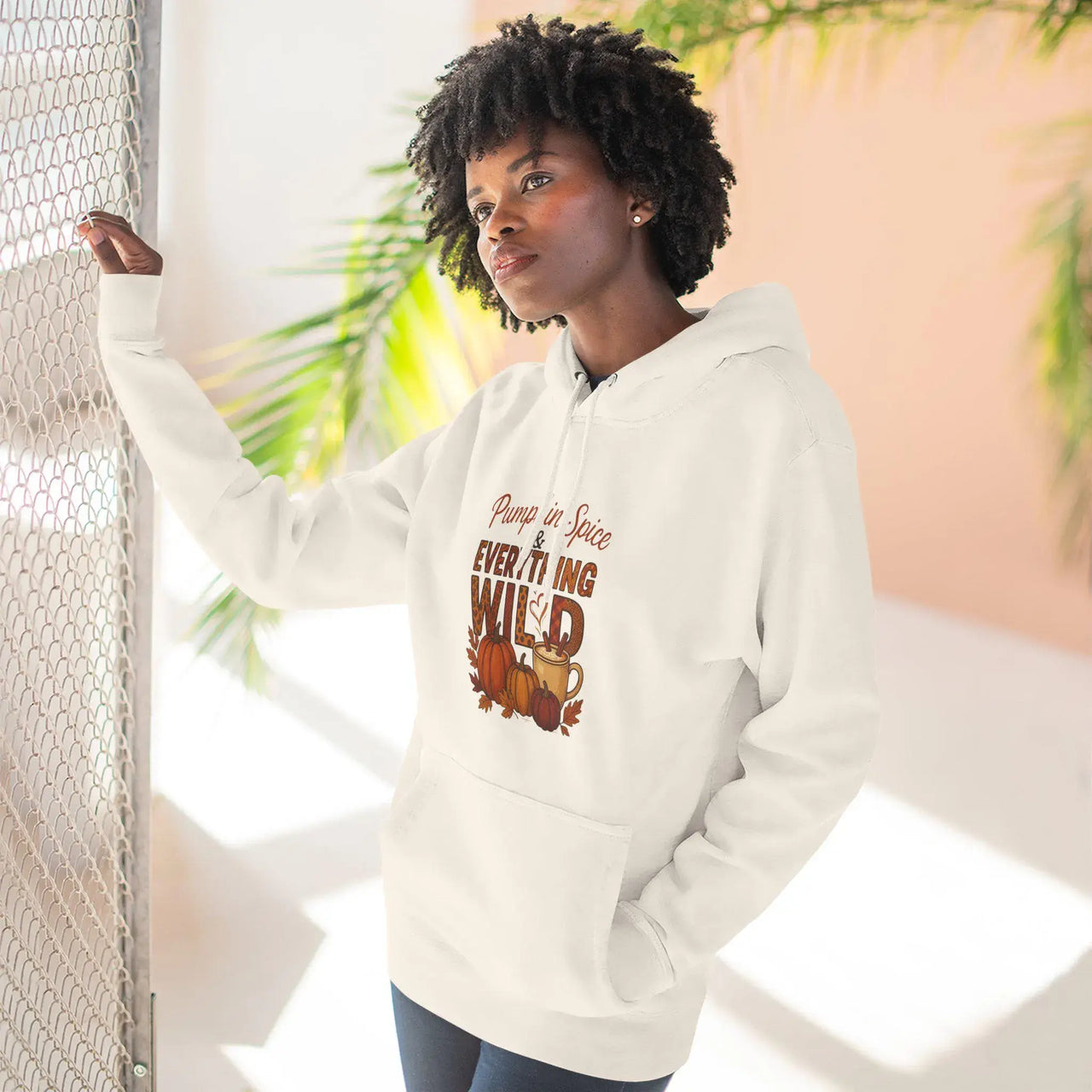 Person wearing a white hoodie with a graphic design, standing indoors with plants in the background.