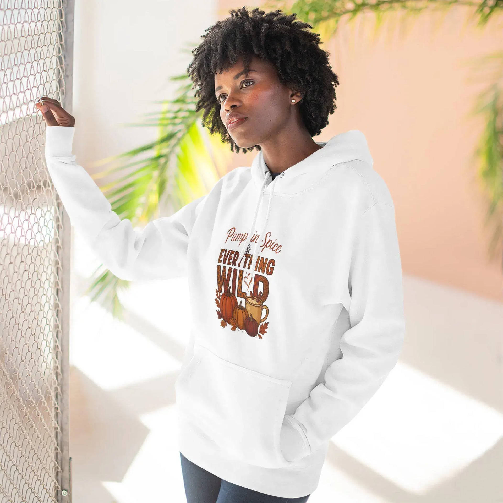 Person wearing a white hoodie with a graphic design, standing against a light-colored wall with plants.